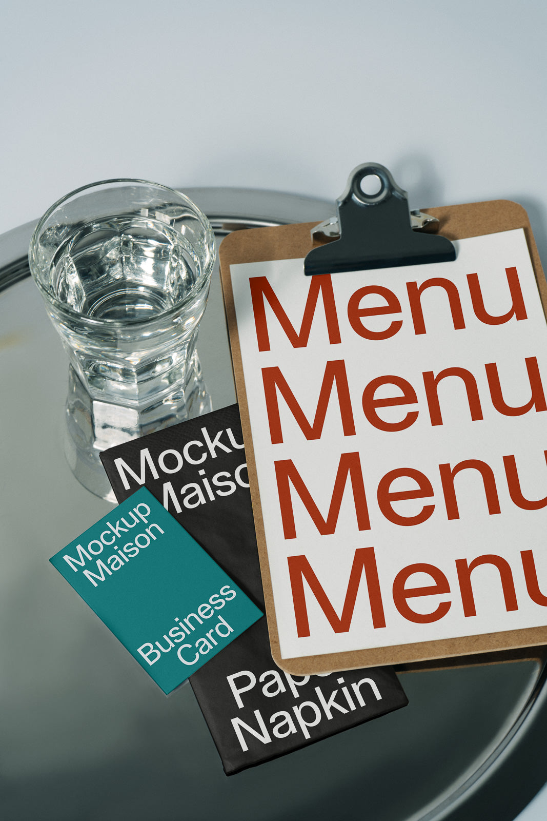 PSD mockup of a clipboard with a menu, next to a glass of water, paper napkin, and business card on a reflective surface.
