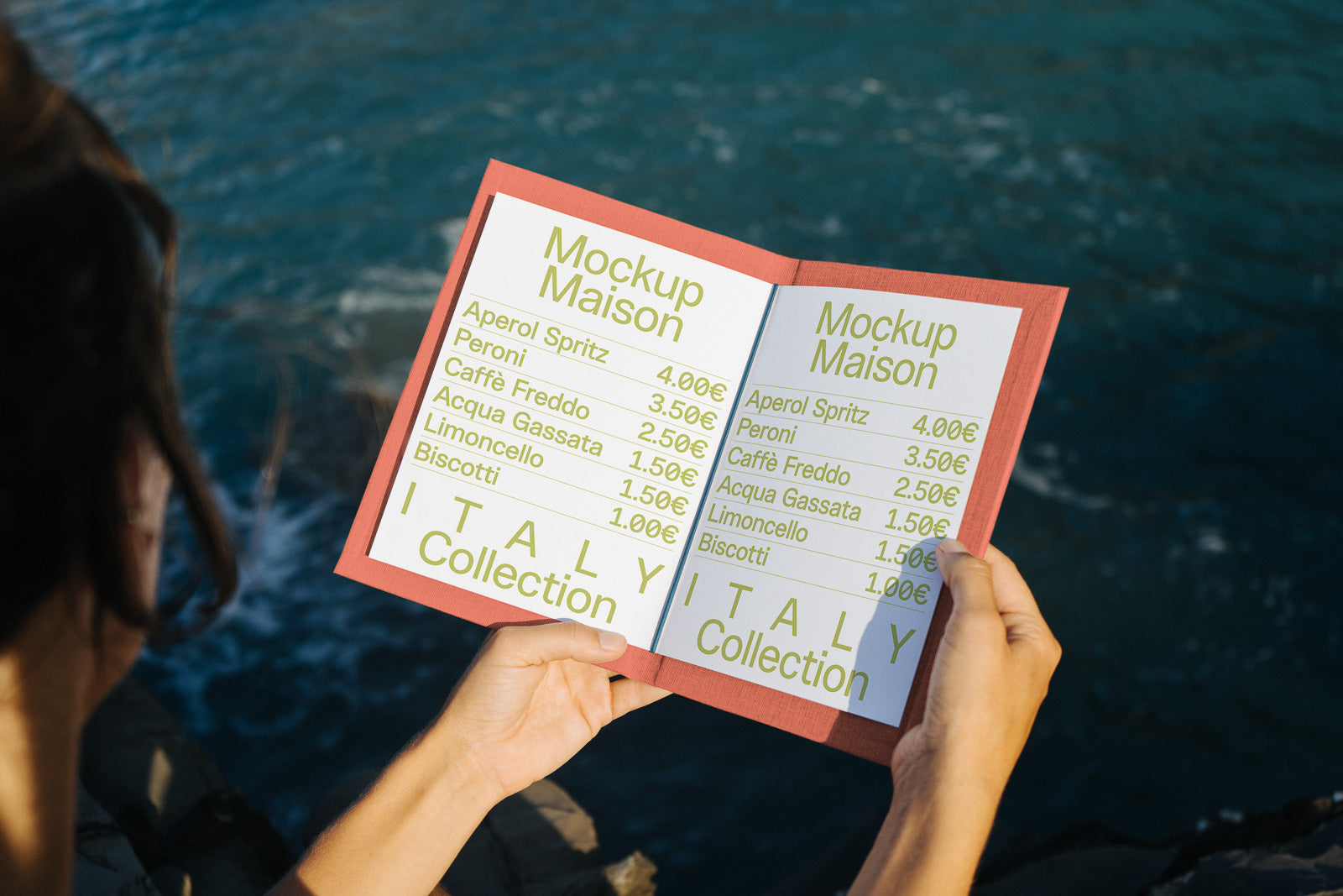 PSD mockup of an open menu held by hands with an ocean backdrop, displaying drink and snack prices, titled "Mockup Maison" and "ITALY Collection."