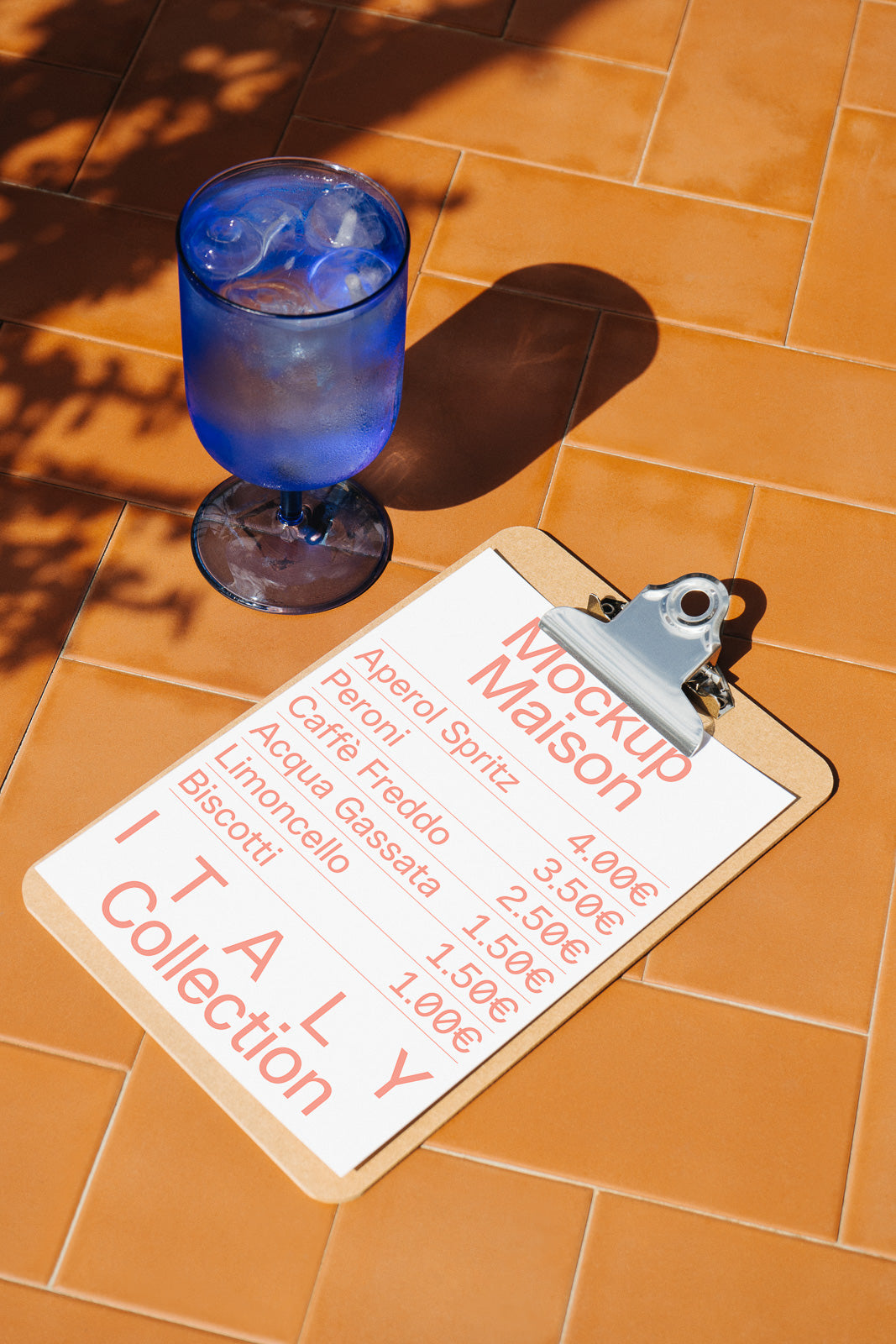 PSD mockup of a clipboard menu displaying beverage prices, placed on terracotta tiles beside a blue glass filled with ice water.