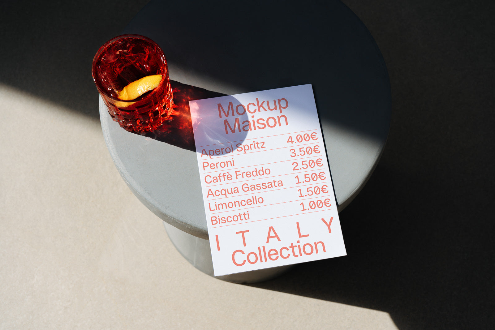 PSD mockup of a menu card featuring drinks and prices, placed on a round gray table next to a red crystal glass with an orange slice.
