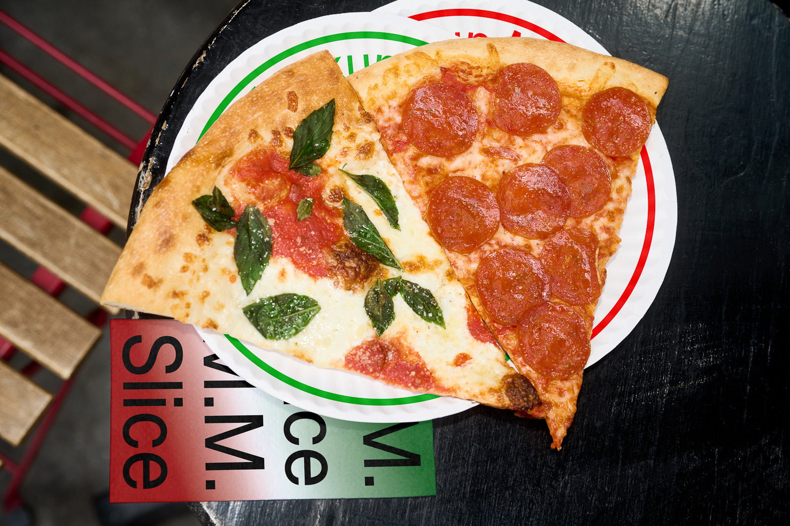 PSD mockup of two pizza slices on a round plate, one with pepperoni and the other with tomato and basil, placed on a black surface.