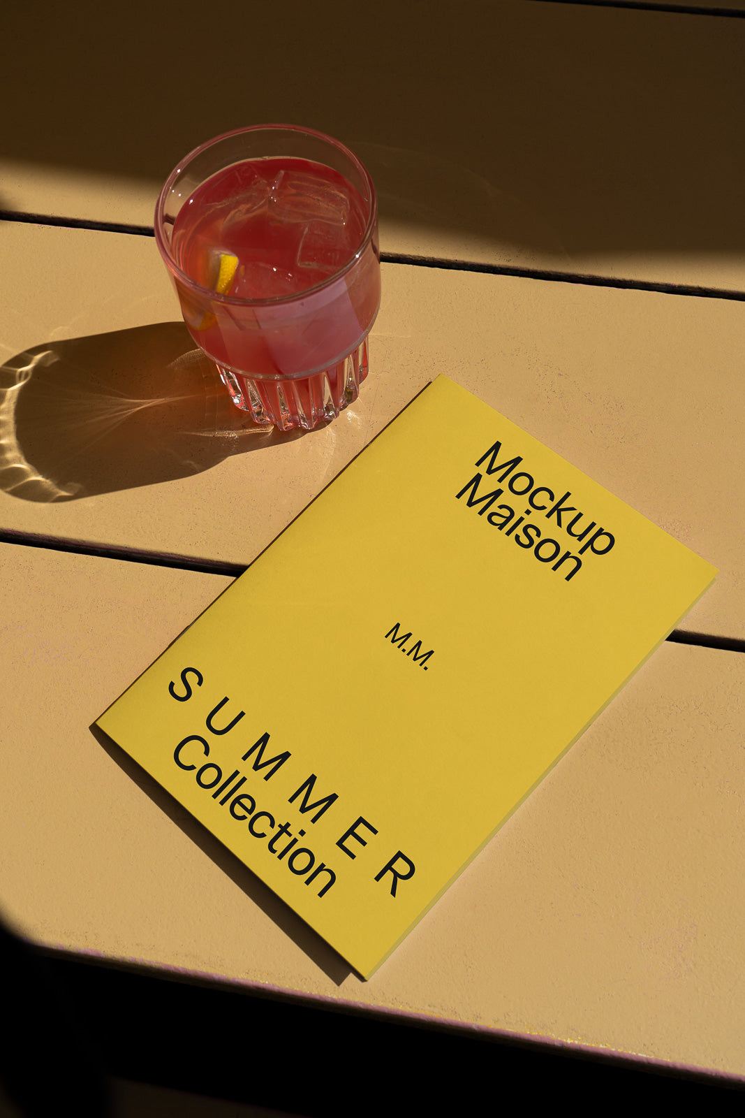 PSD mockup of a yellow "Summer Collection" booklet on a table beside a pink drink with ice and lemon slice.