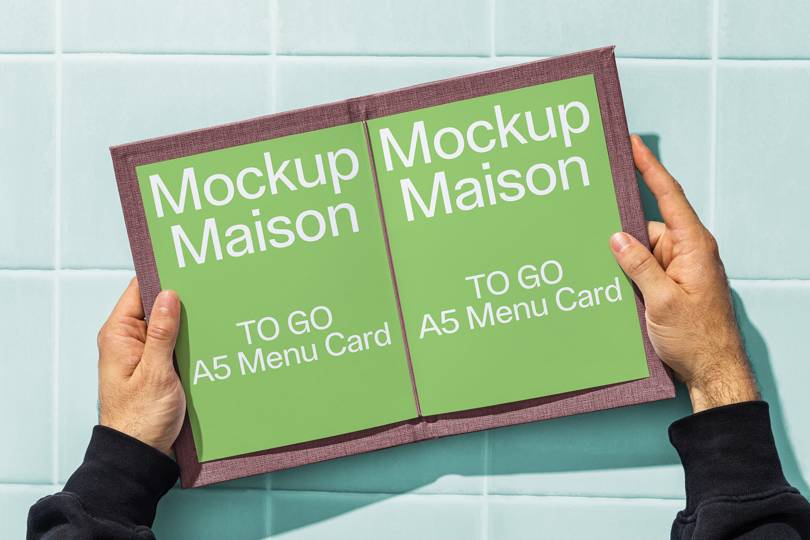 PSD mockup of a person holding an open A5 menu card with a textured cover against a tiled background.