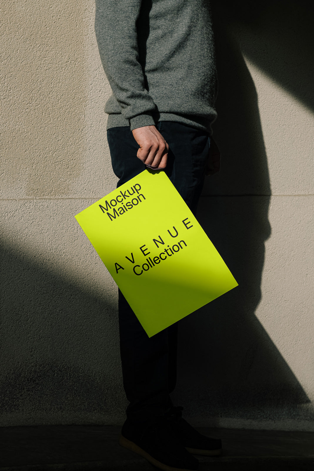 PSD mockup of a person holding a bright yellow poster with black text, partially obscured by shadow, leaning against a textured wall.