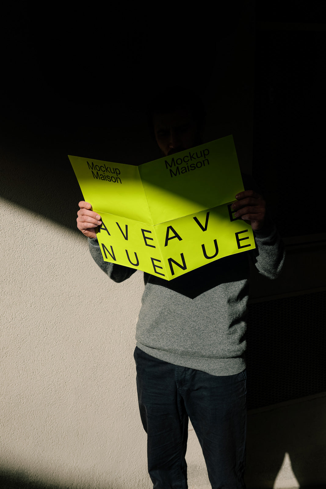 PSD mockup of a person holding a bright yellow booklet with bold black text and "Mockup Maison" printed at the top, against a shaded wall background.