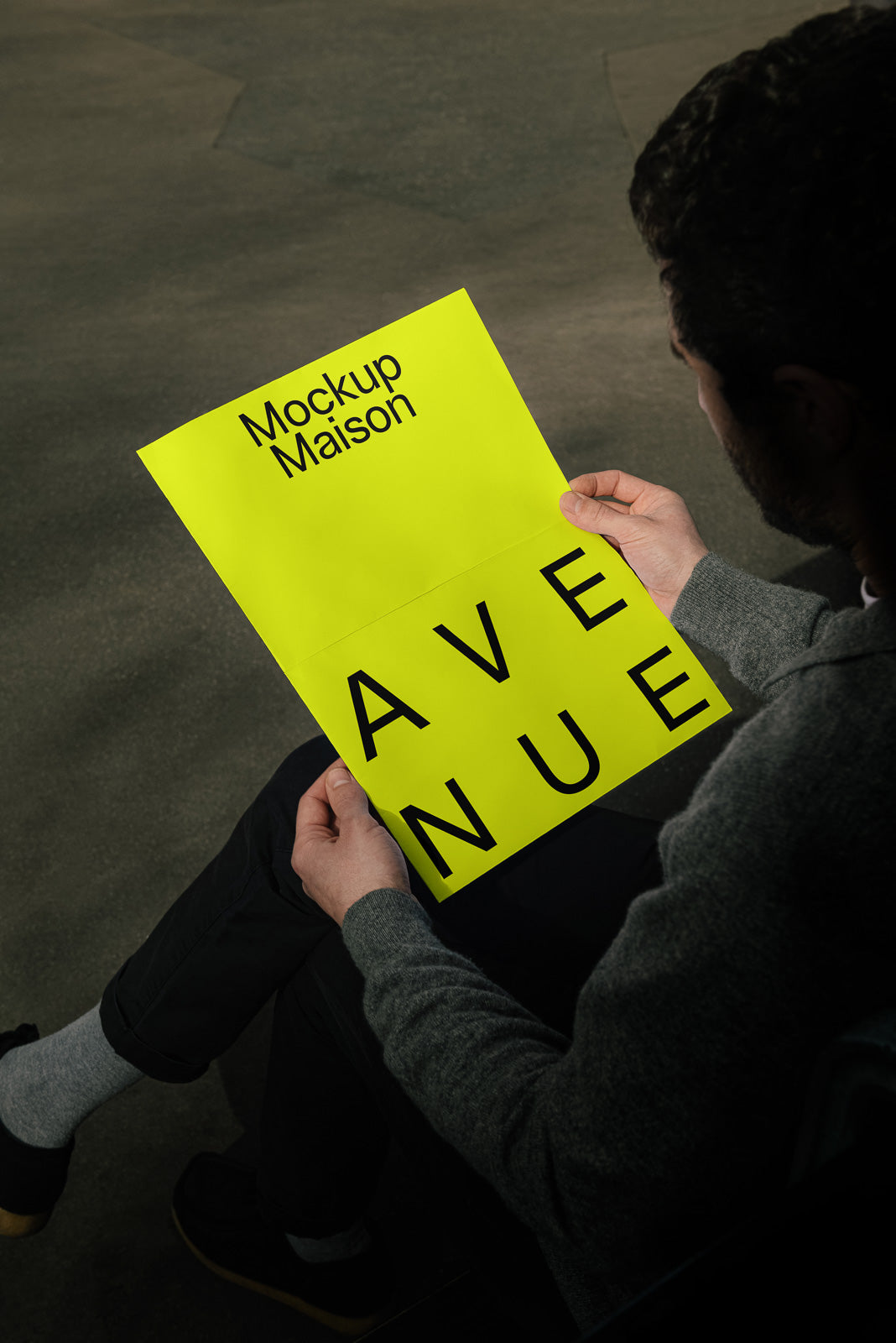 PSD mockup of a person holding a bright yellow paper folder labeled with "Mockup Maison" and "AVENUE" in bold black text, against a dark background.