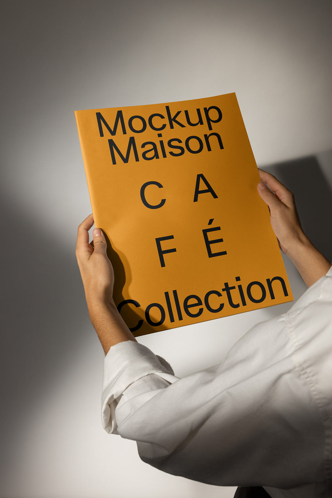 PSD mockup of hands holding an orange book cover that reads "Mockup Maison Café Collection" in bold black letters.