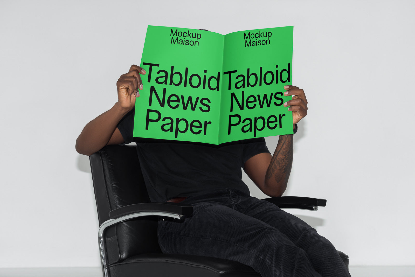 PSD mockup of a person seated on a black chair, holding a green tabloid newspaper with bold black text and "Mockup Maison" branding.