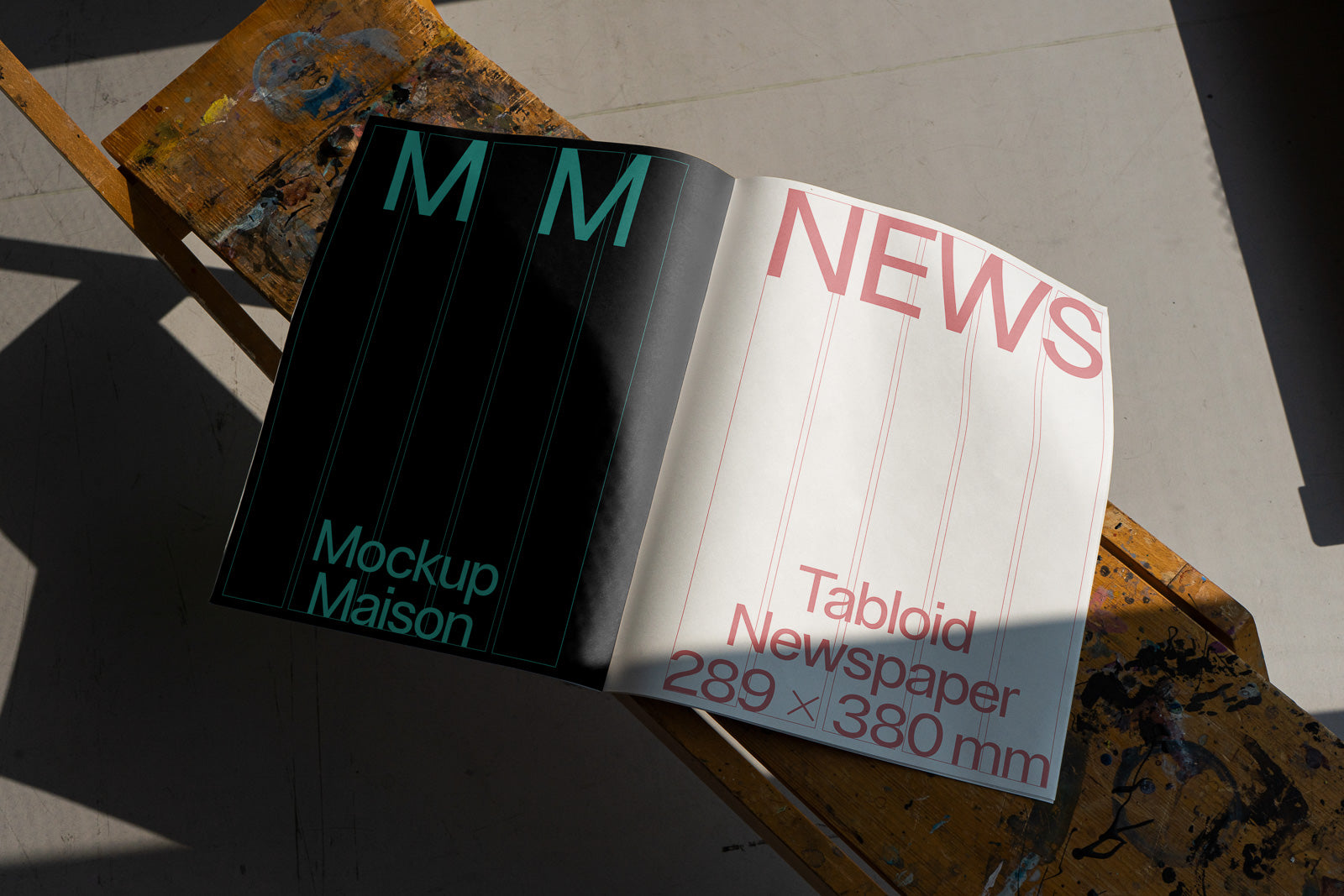 PSD mockup of an open tabloid newspaper on a wooden chair, displaying bold typography on black and white pages marked with grid lines.