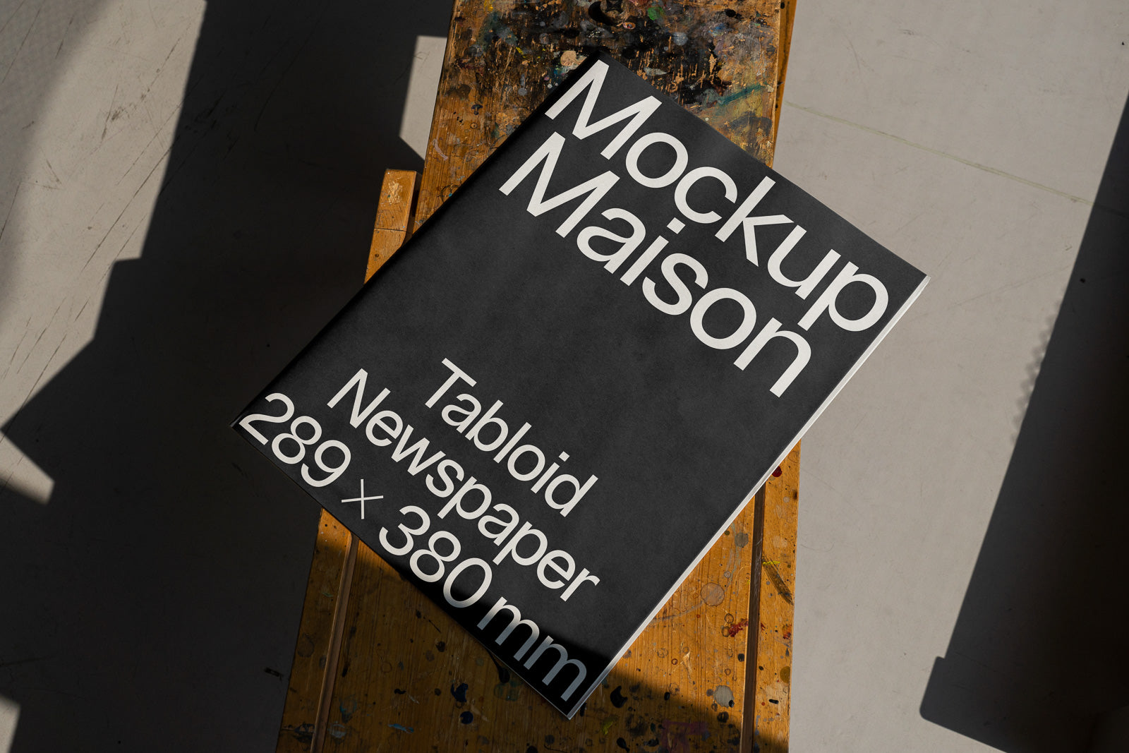 PSD mockup of a tabloid newspaper with dimensions 289 x 380 mm on a textured wooden surface, placed under natural light with shadows.