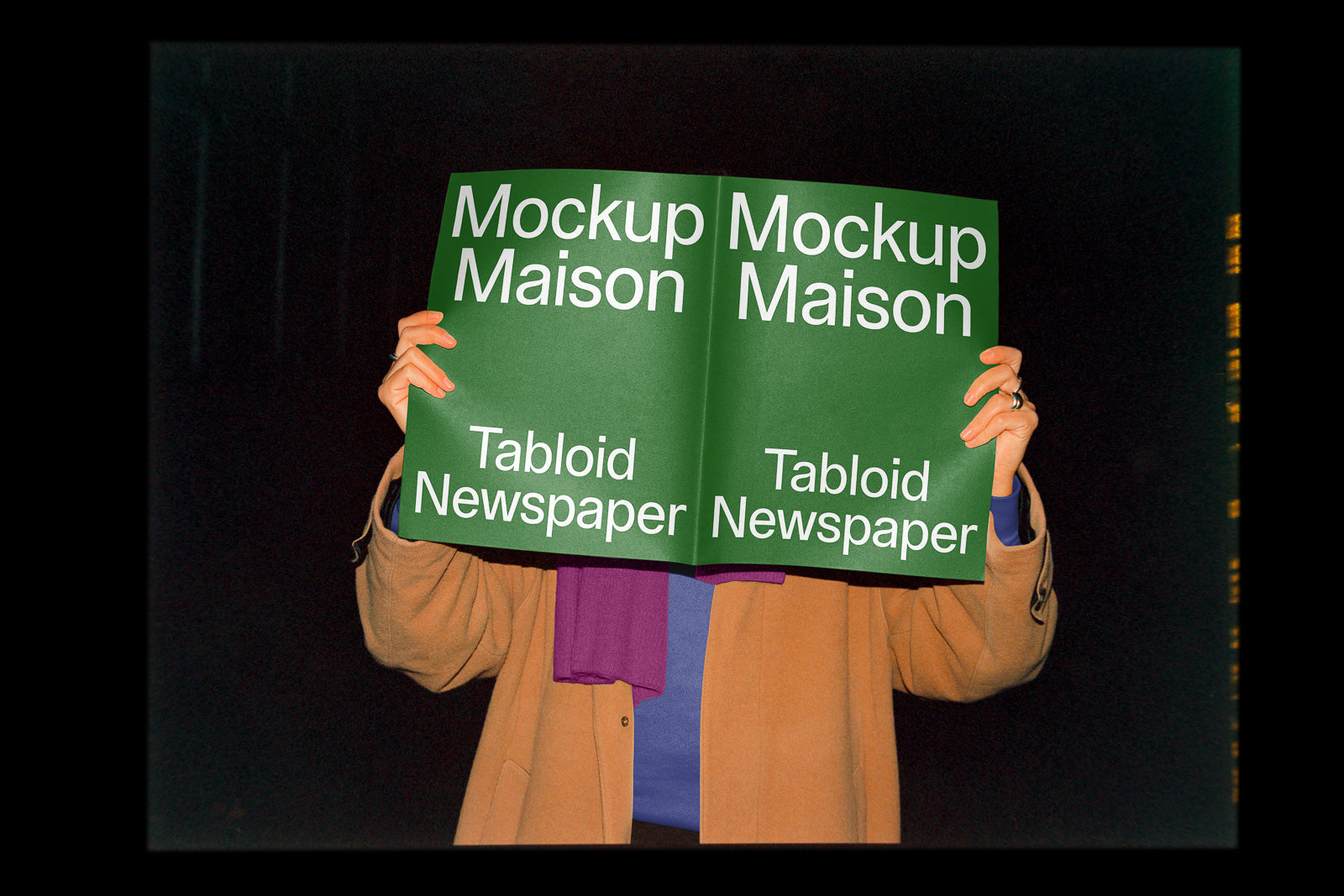 PSD mockup of a person holding an open tabloid newspaper with green covers and white text "Mockup Maison Tabloid Newspaper" visible, set against a dark background.