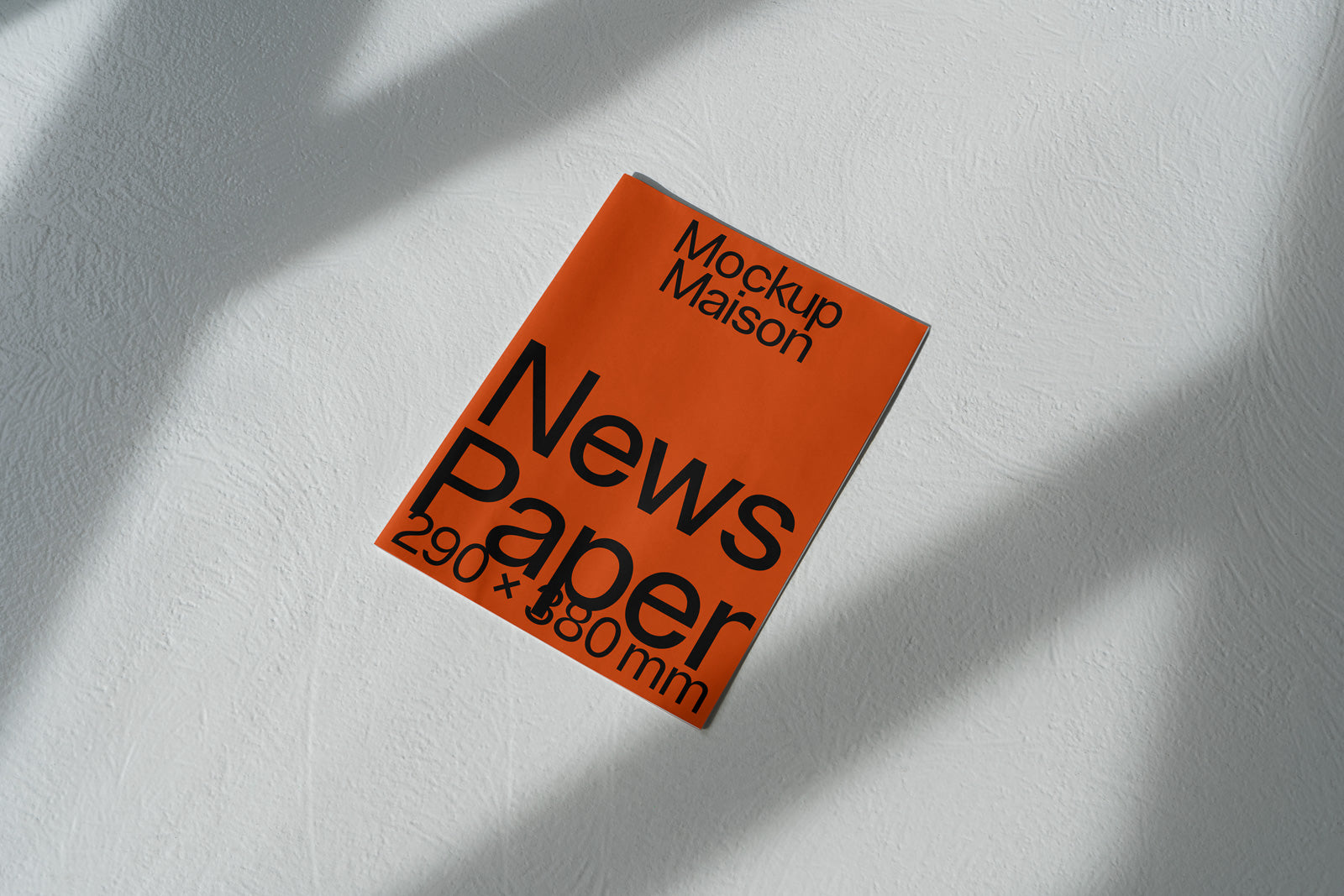 PSD mockup of an orange newspaper on a textured white surface, titled "Mockup Maison News Paper 290 x 380 mm" with shadows casting across it.