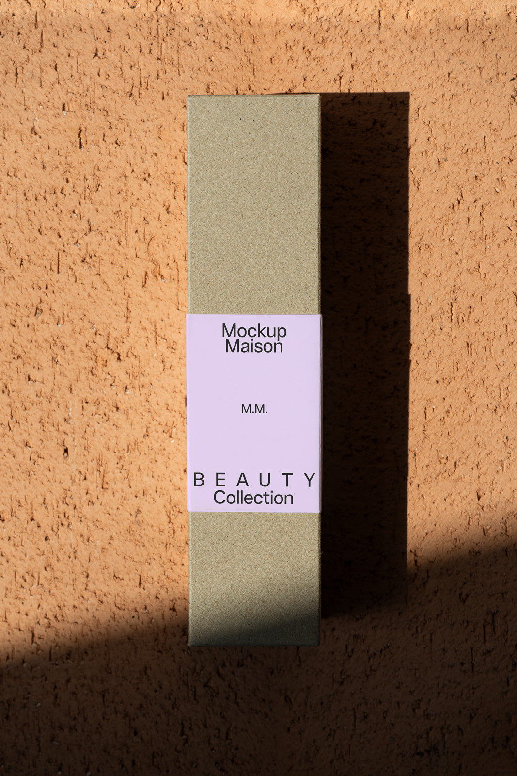 PSD mockup of a rectangular packaging box labeled "Mockup Maison Beauty Collection" leaning against a textured, sunlit beige wall.