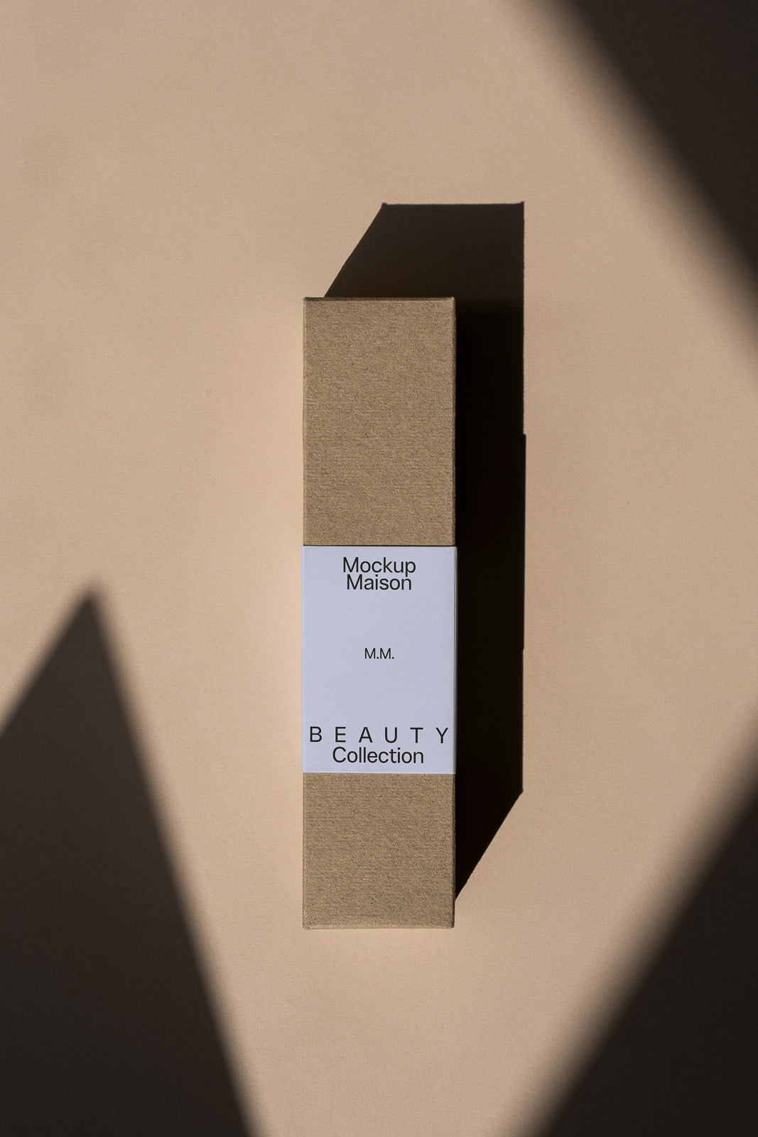 PSD mockup of a rectangular, cardboard box with a minimalist label reading "Mockup Maison Beauty Collection" on a beige background. Shadows cast diagonally.