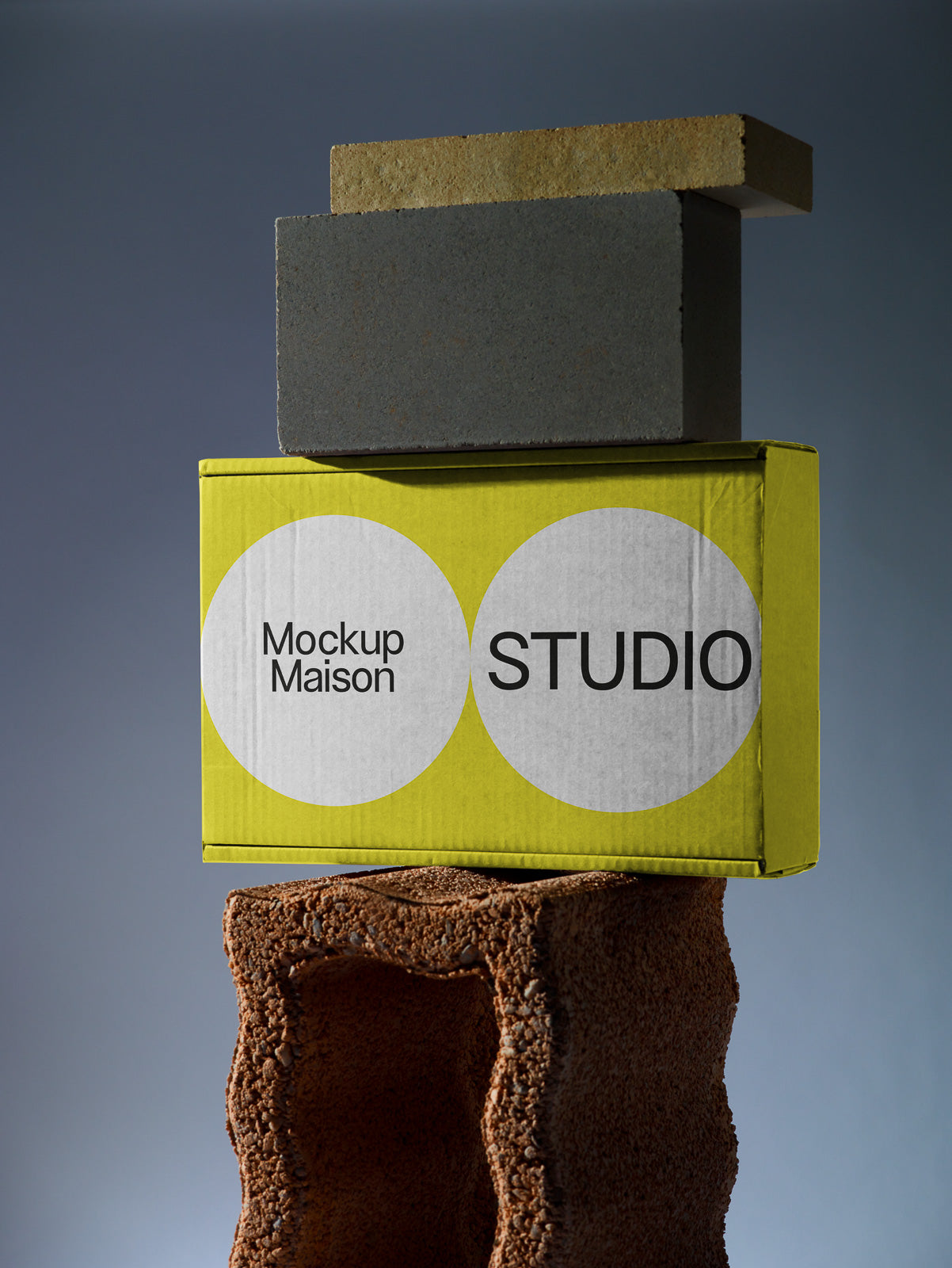 PSD mockup of a stack featuring a yellow box labeled "Mockup Maison Studio," sandwiched between a textured brown hollow block and two bricks.