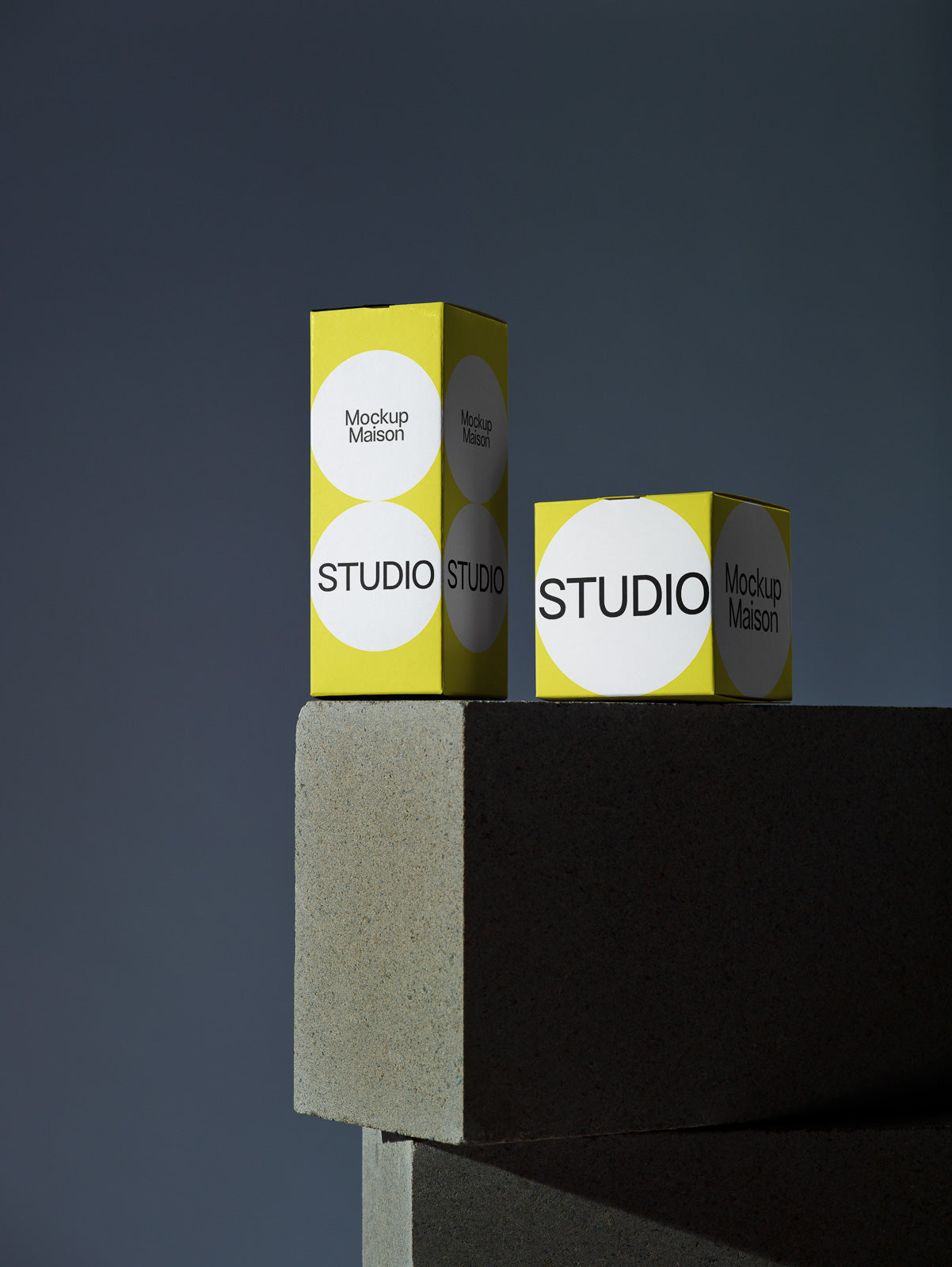 PSD mockup of two yellow and white Studio-branded boxes in a minimalist setting on stacked concrete blocks.