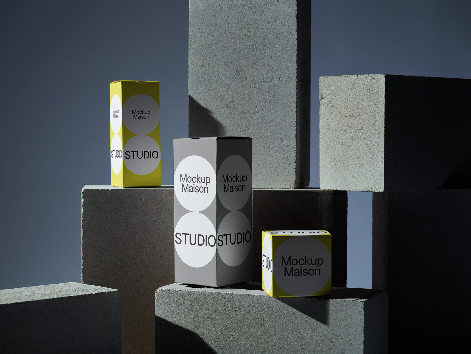 PSD mockup of three rectangular boxes with "Mockup Maison" and "Studio" text, arranged on concrete blocks against a dark background.