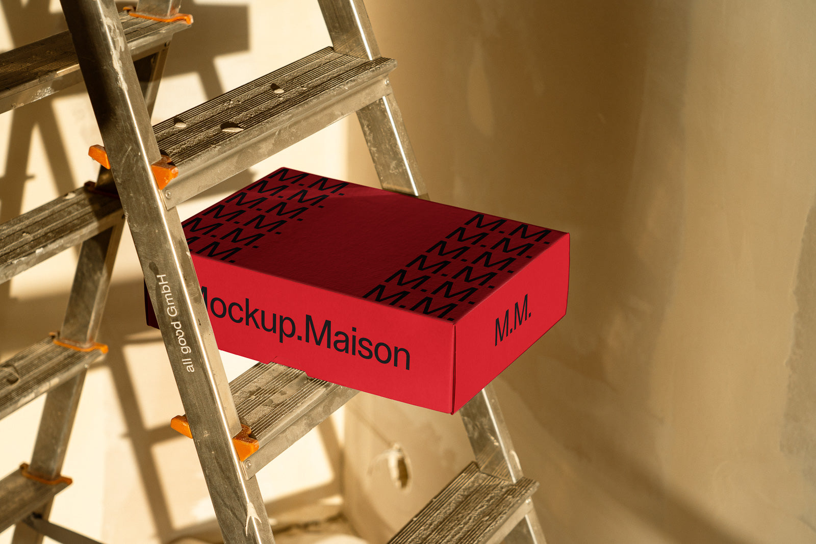 PSD mockup of a red box labeled "M.M." placed on a metal stepladder with sunlight casting shadows on the wall in the background.