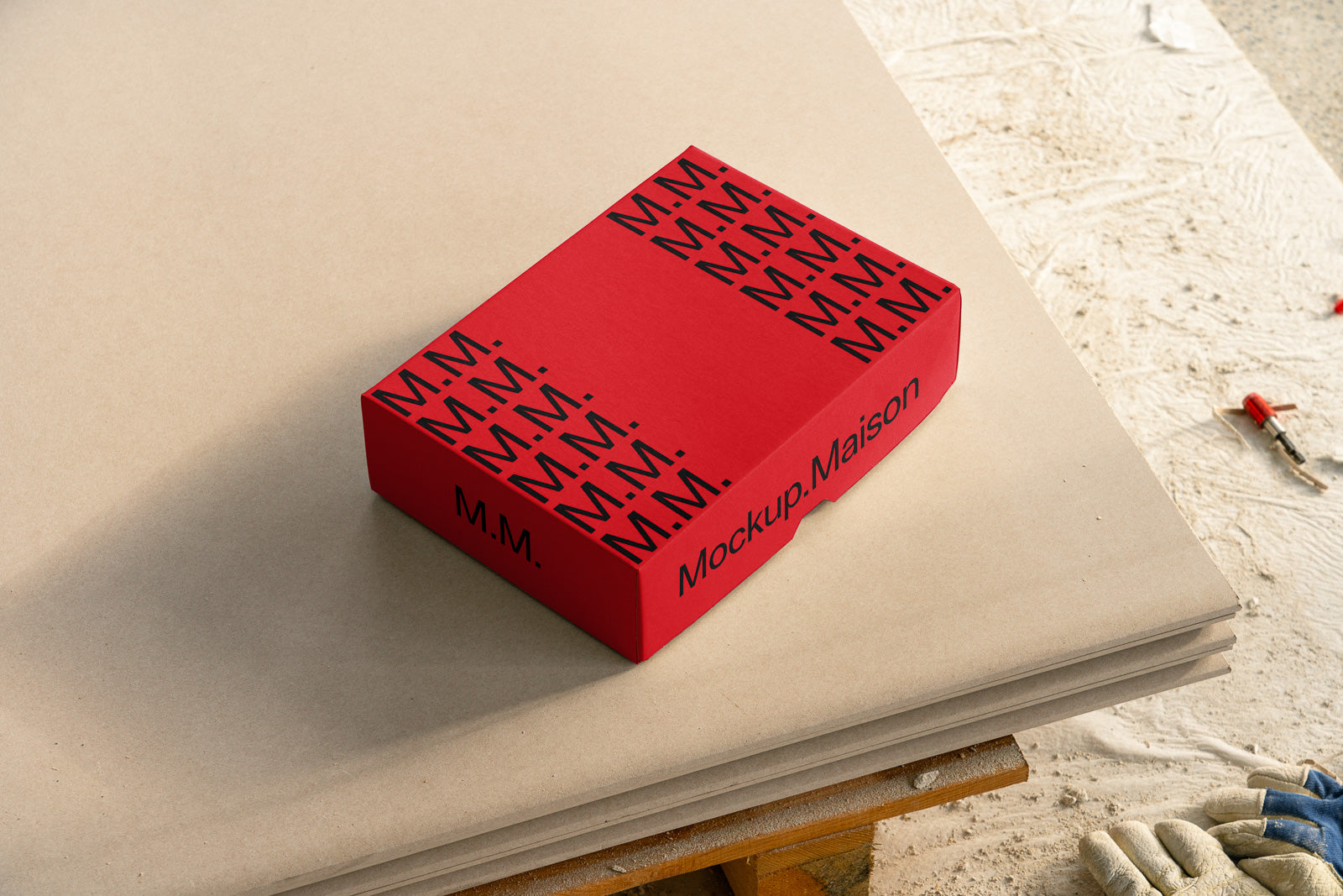 PSD mockup of a red rectangular box with "M.M." and "Mockup Maison" text, placed on stacked sheets of thick paper on a wooden surface.