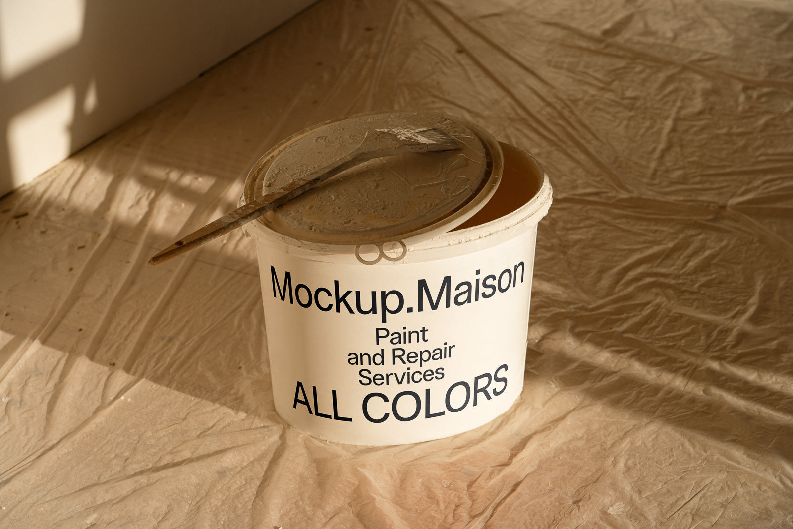 PSD mockup of a paint container labeled "Mockup.Maison Paint and Repair Services All Colors" with a paintbrush resting on its lid.