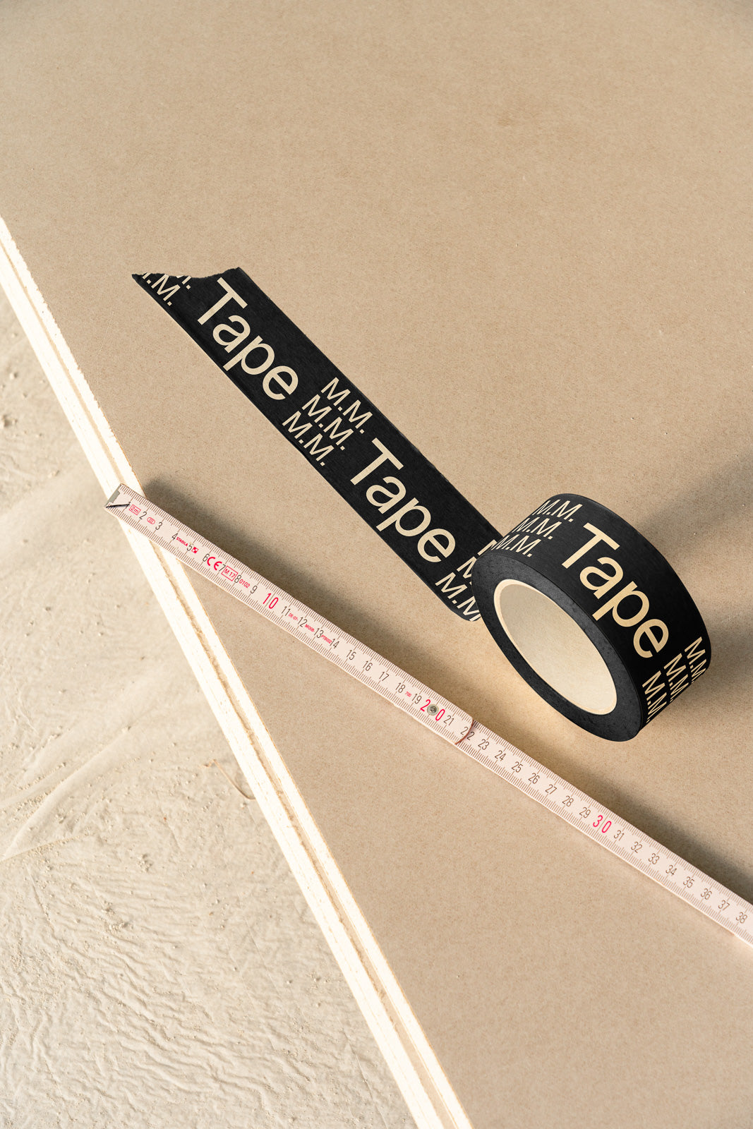 PSD mockup of black tape roll with "Tape" text and a white measuring tape on a beige surface.