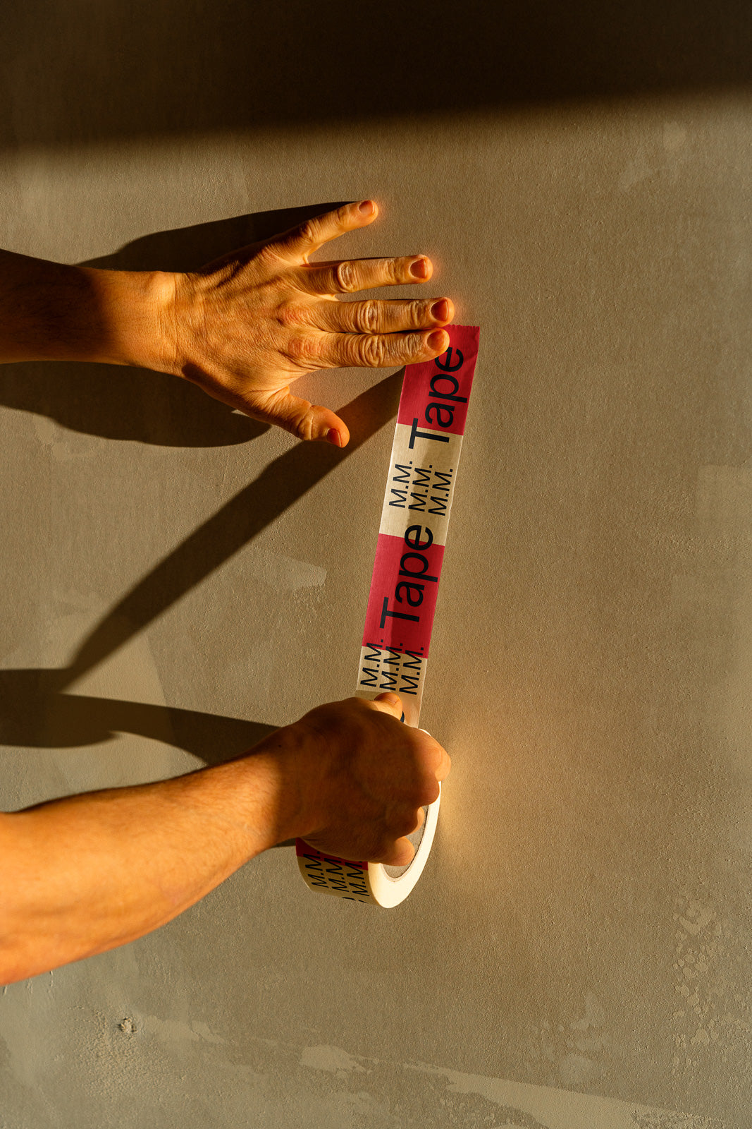 PSD mockup of hands applying branded tape on a wall in warm lighting, showcasing texture and shadow details.