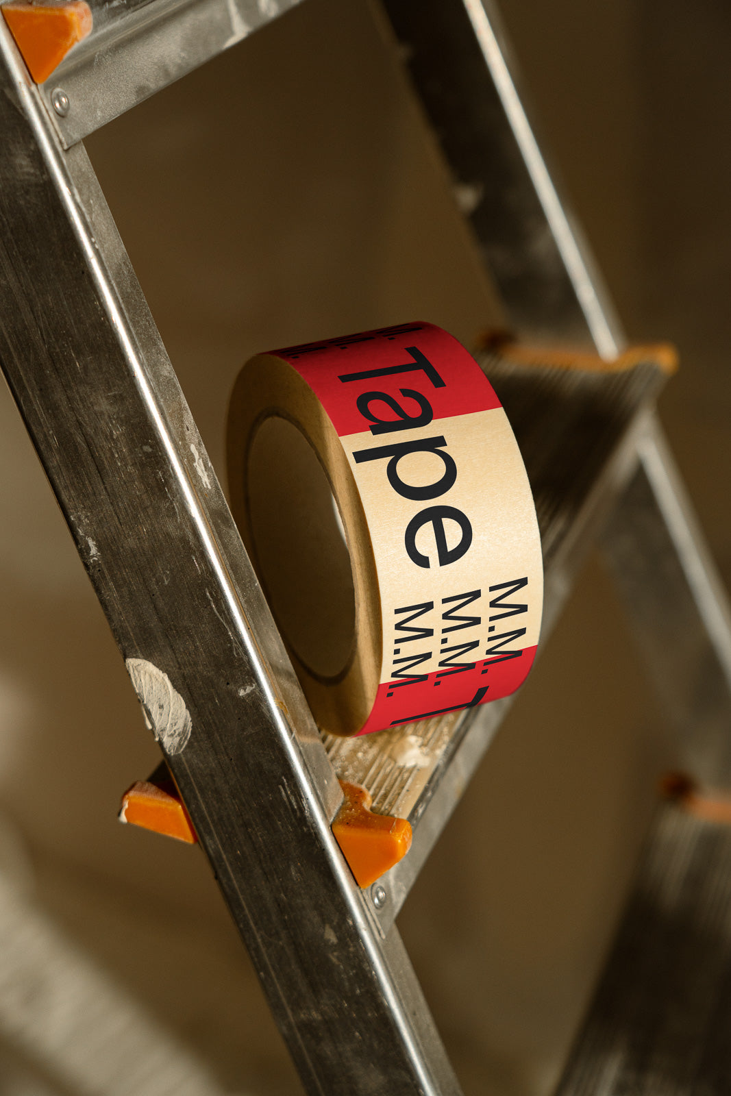 PSD mockup of a roll of branded tape resting on a metal ladder, featuring a red and beige design with bold black text.