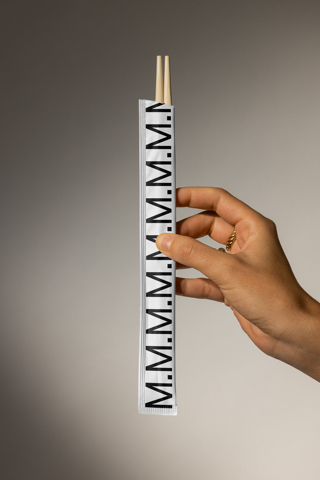 PSD mockup of a hand holding chopsticks in a branded sleeve with black typography on a neutral background.