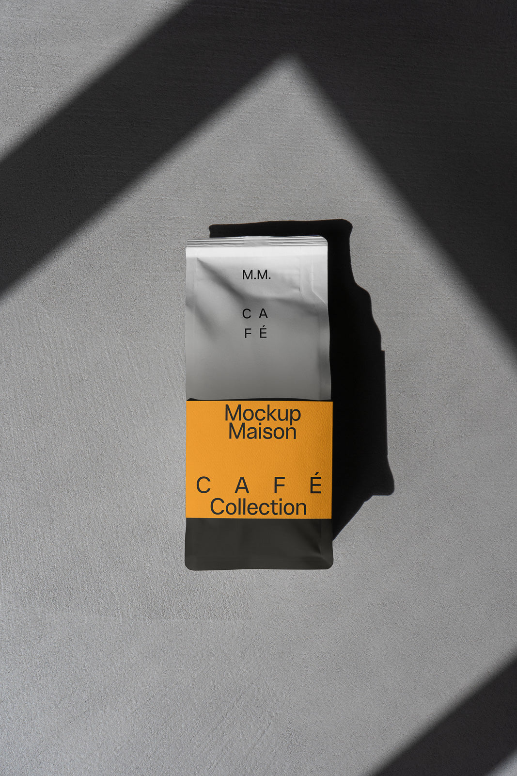 PSD mockup of a café coffee bag with a gray and orange design, labeled "Mockup Maison Café Collection" against a textured surface and shadowed lighting.