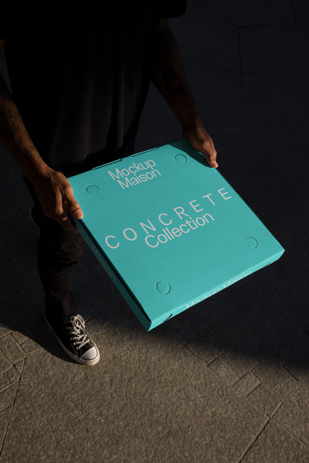 PSD mockup of a person holding a turquoise box labeled "Mockup Maison CONCRETE Collection" with a shadowy background.