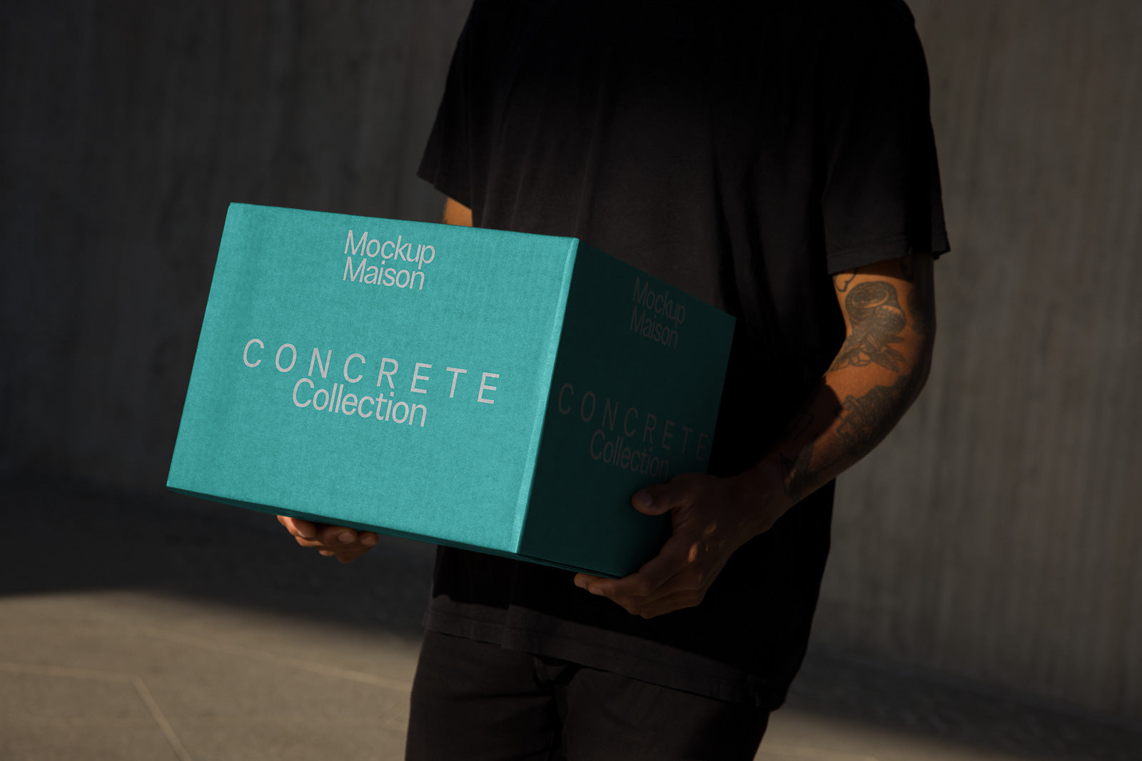 PSD mockup of a person holding a turquoise box labeled "Mockup Maison Concrete Collection" with shadowed lighting accentuating details.
