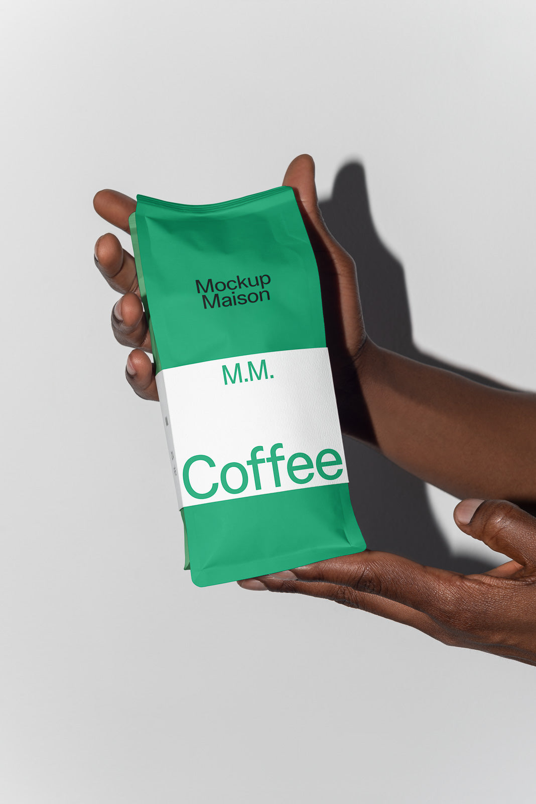 PSD mockup of a green coffee bag labeled "Mockup Maison" and "M.M. Coffee," held by two hands against a neutral background.