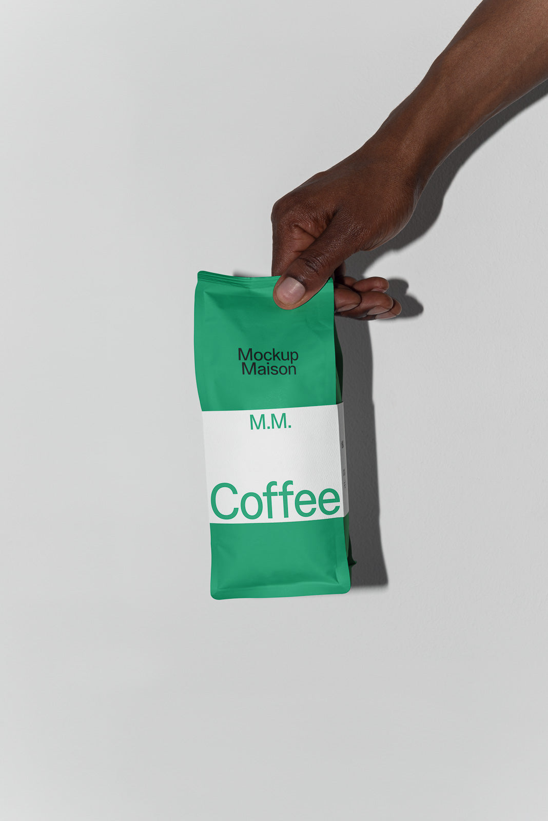 PSD mockup of a hand holding a green and white bag labeled "M.M. Coffee" with "Mockup Maison" branding against a plain background.