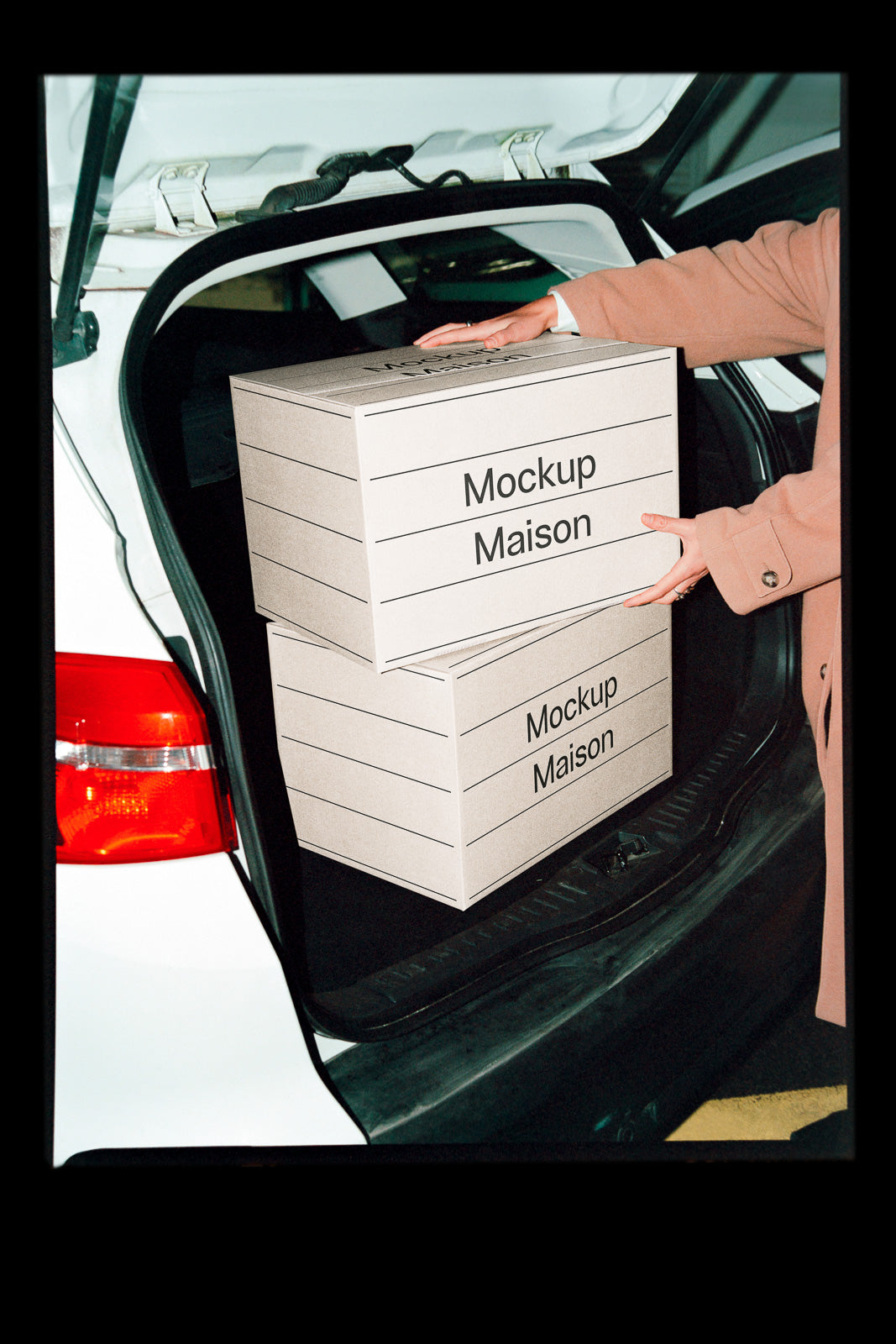 PSD mockup of two cardboard boxes labeled "Mockup Maison" being placed in the trunk of a white car by a person wearing a beige coat.