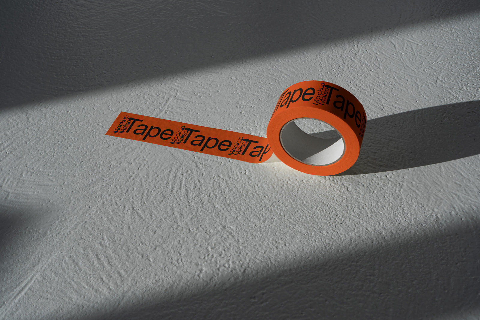 PSD mockup of an orange roll of tape with black text, partially unrolled on a textured gray surface, casting a shadow.