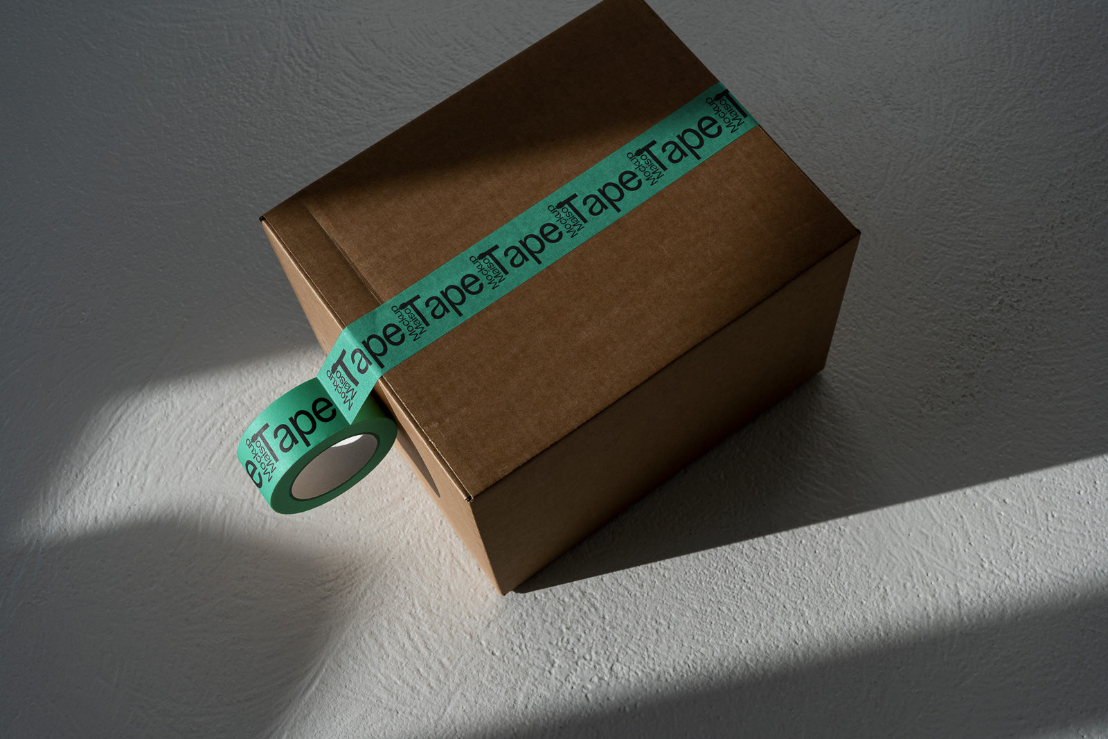 PSD mockup of a brown cardboard box sealed with green tape featuring bold black text, casting a shadow on a textured white surface.