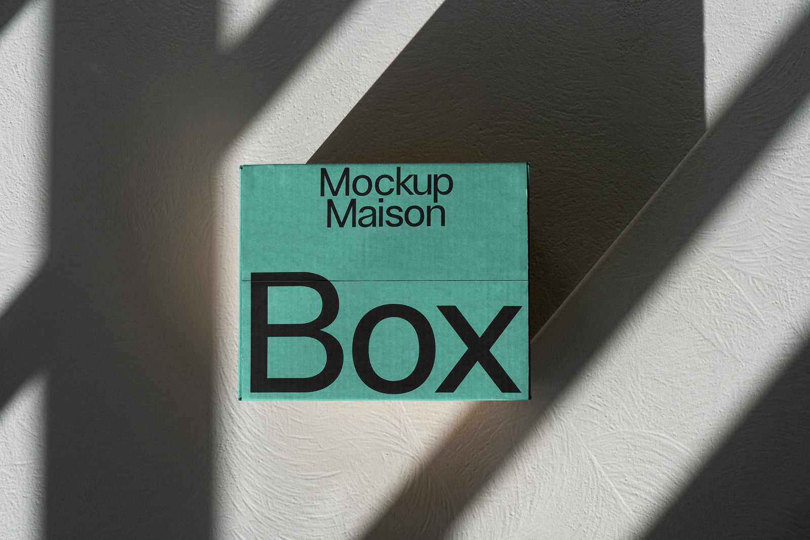 PSD mockup of a teal box labeled "Mockup Maison" and "Box" against a textured wall with diagonal shadow patterns.