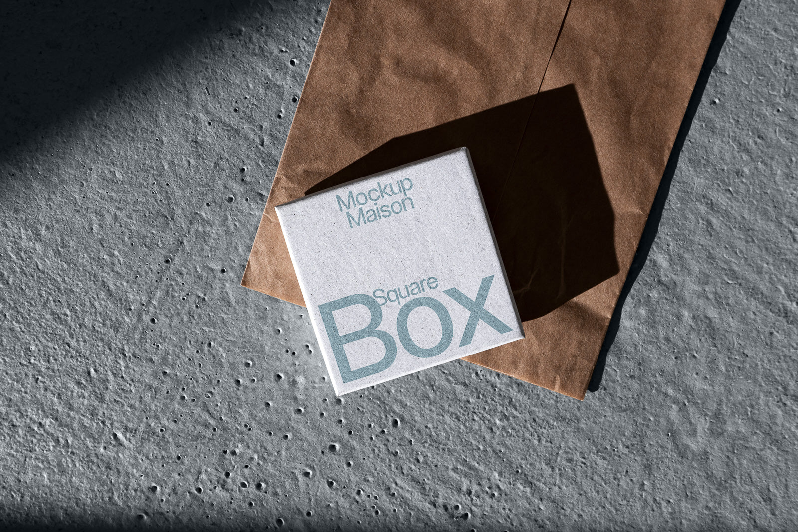 PSD mockup of a square box featuring the text "Mockup Maison Square Box," placed atop a crumpled brown paper on a textured surface.