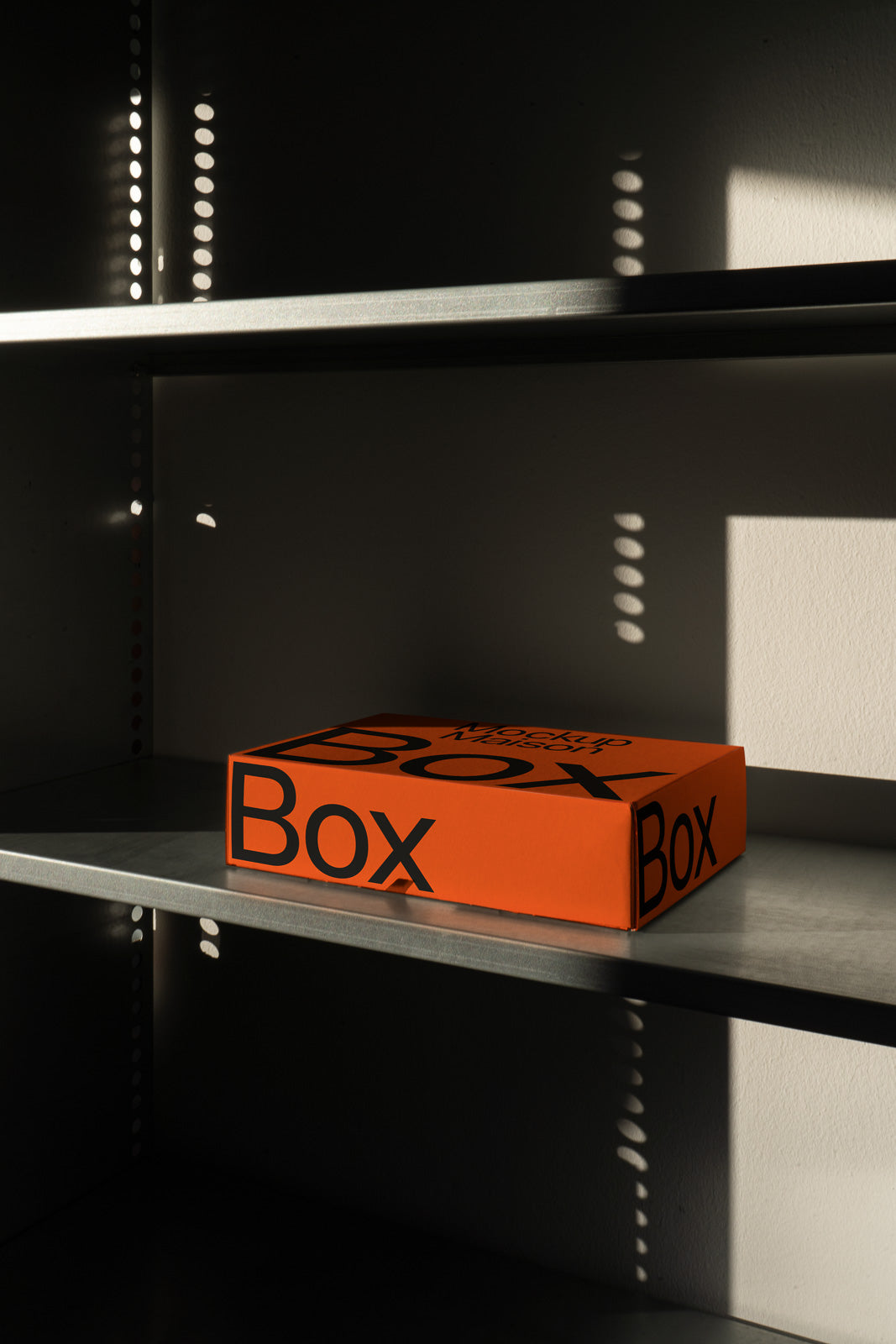 PSD mockup of an orange box with bold black text, placed on a metal shelf in a dimly lit setting with light and shadow interplay.