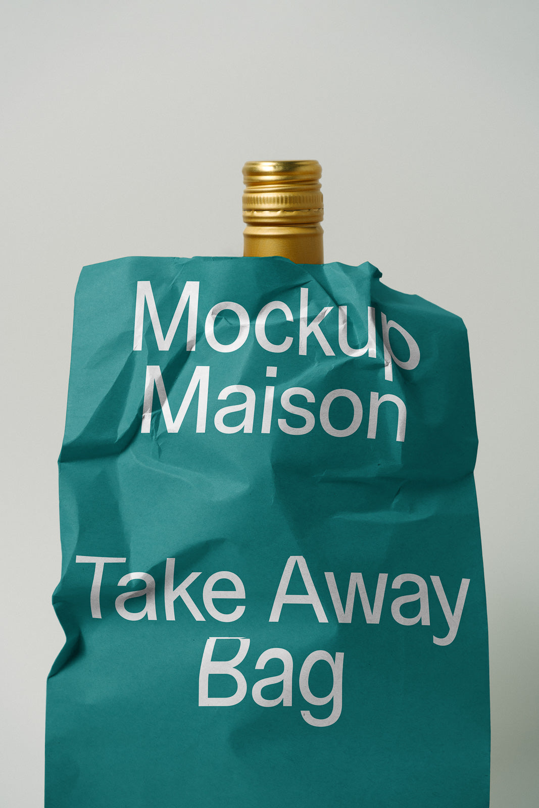 PSD mockup of a crumpled teal paper bag labeled "Mockup Maison Take Away Bag" partially covering a gold bottle cap.