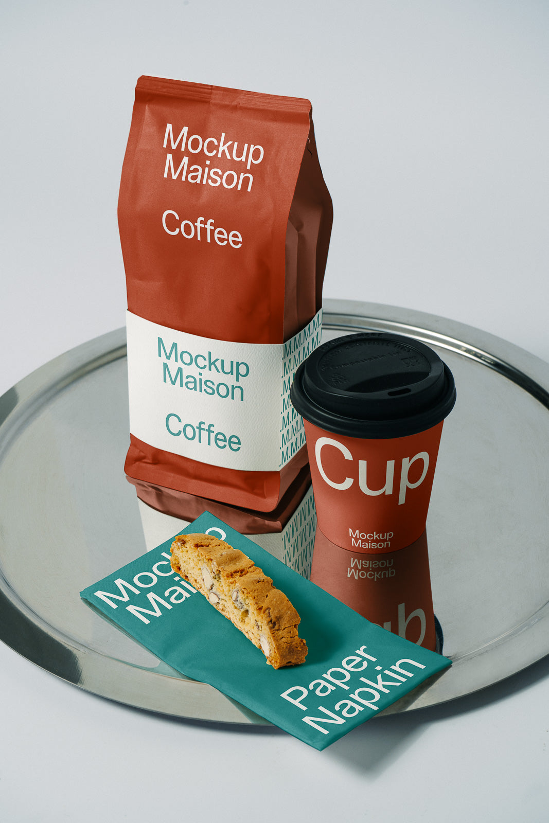 PSD mockup of coffee bag, branded cup, napkin with biscotti on a reflective tray, highlighting packaging design and branding elements.