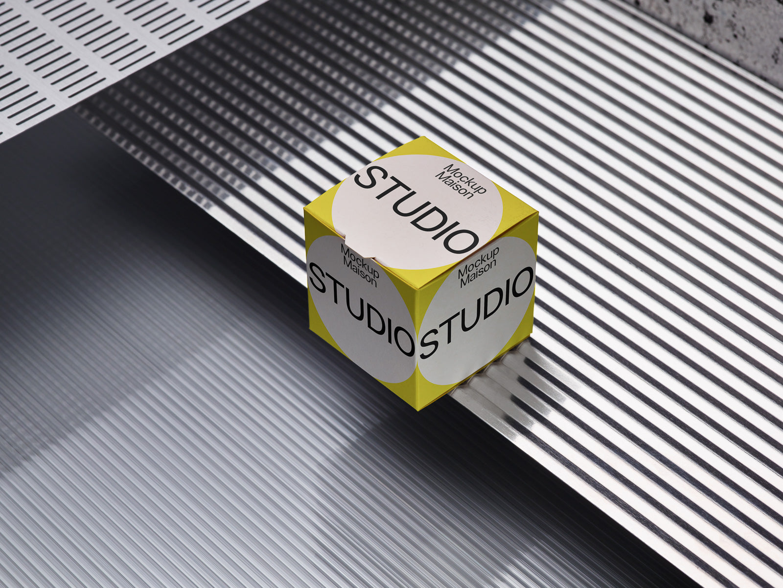 PSD mockup of a yellow and white cube on a striped reflective surface, displaying the text "Mockup Maison Studio" on each visible side.