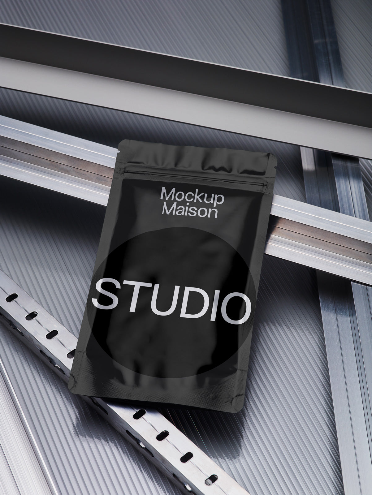 PSD mockup of a black pouch labeled "Mockup Maison STUDIO" resting on intersecting metallic surfaces.