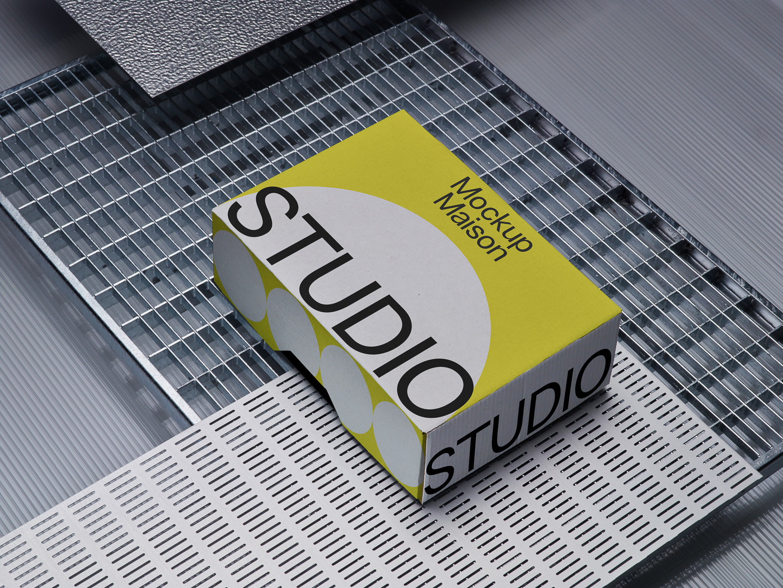 PSD mockup of a rectangular box with bold text reading “STUDIO” on a textured metal surface. The box design features yellow and gray patterns.