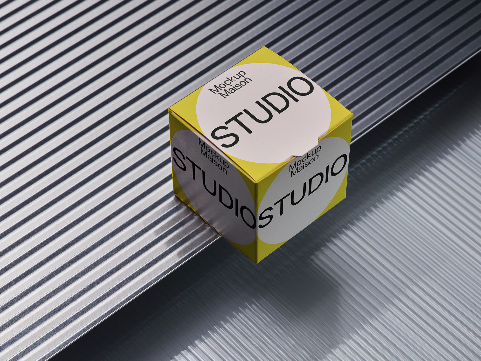 PSD mockup of a yellow cube with the word "STUDIO" printed on white circles, placed on metallic, textured surfaces with diagonal lines.