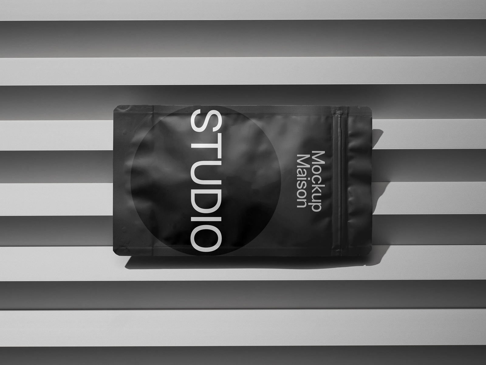 PSD mockup of a black packaging pouch with the text "Studio" and "Mockup Maison" on a textured, striped background.