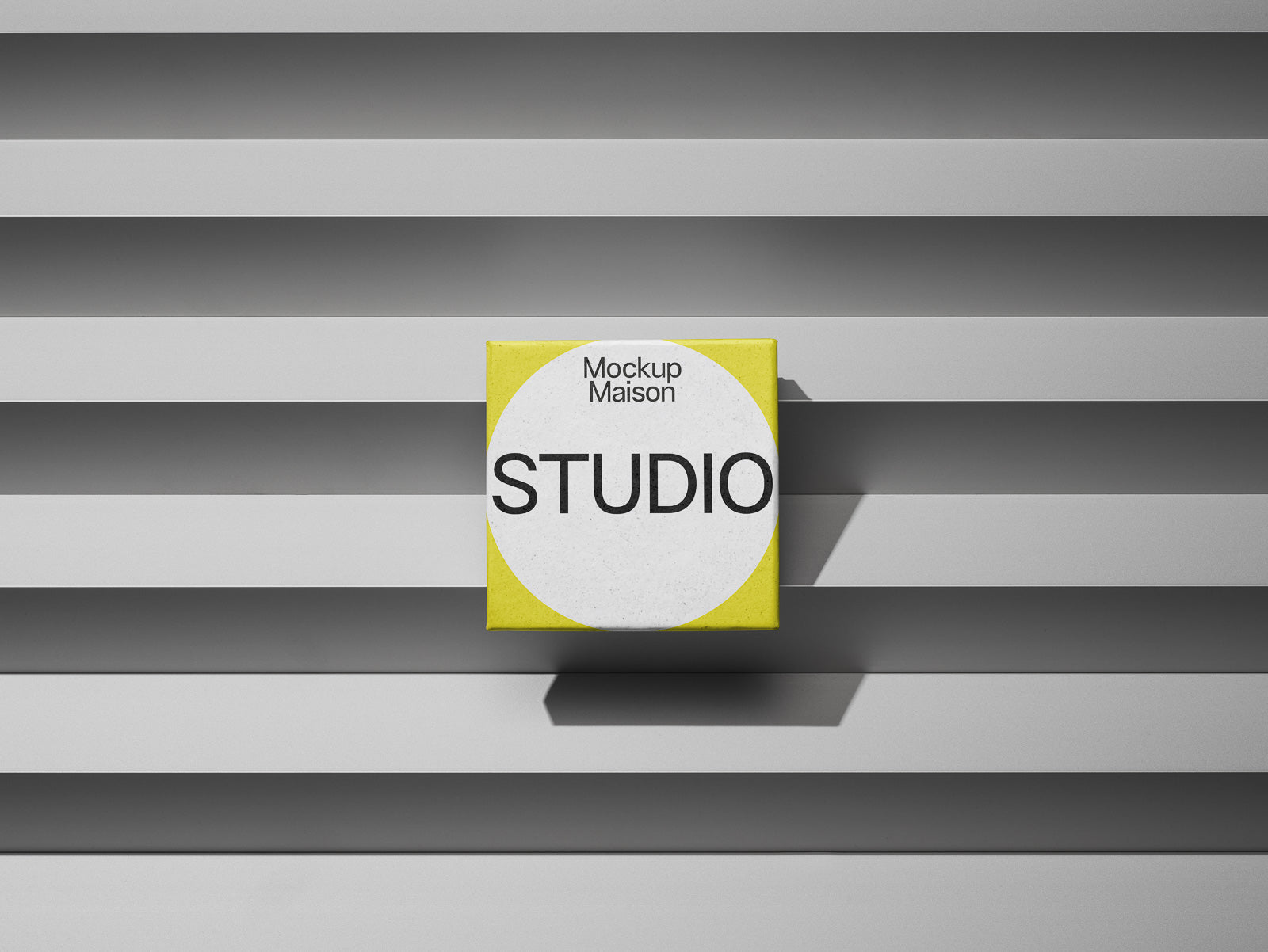 PSD mockup of a square package labeled "Mockup Maison STUDIO," placed on a gray horizontal striped background with a shadow effect.