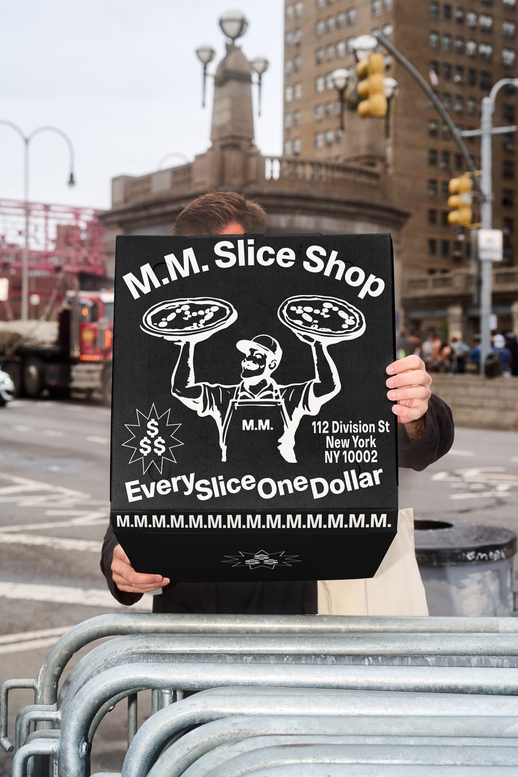 PSD mockup of a person holding a large pizza box with graphics and text advertising "M.M. Slice Shop" on an urban street background.