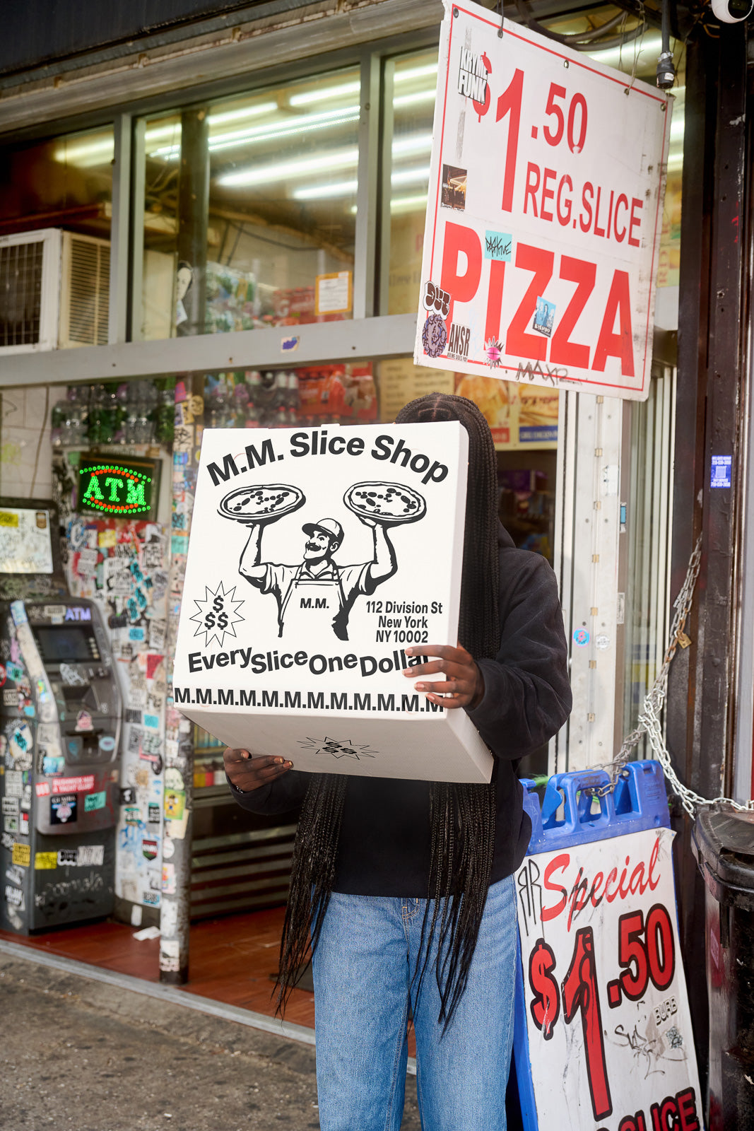 PSD mockup of a person holding a large pizza box outside a shop with signage advertising $1.50 pizza slices.