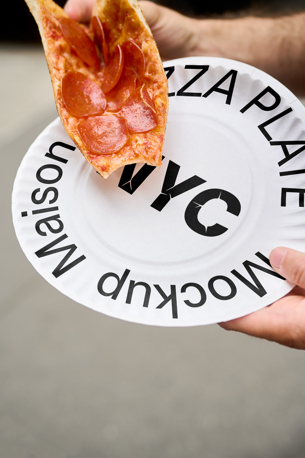 PSD mockup of a white plate with bold black text, held by a hand, underneath a slice of pepperoni pizza being folded.